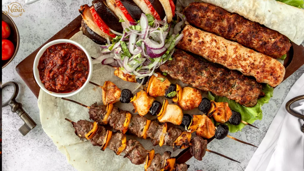Overhead view of a Persian mixed kebab plate featuring Koobideh, marinated chicken skewers, flatbread, and fresh side dishes.
