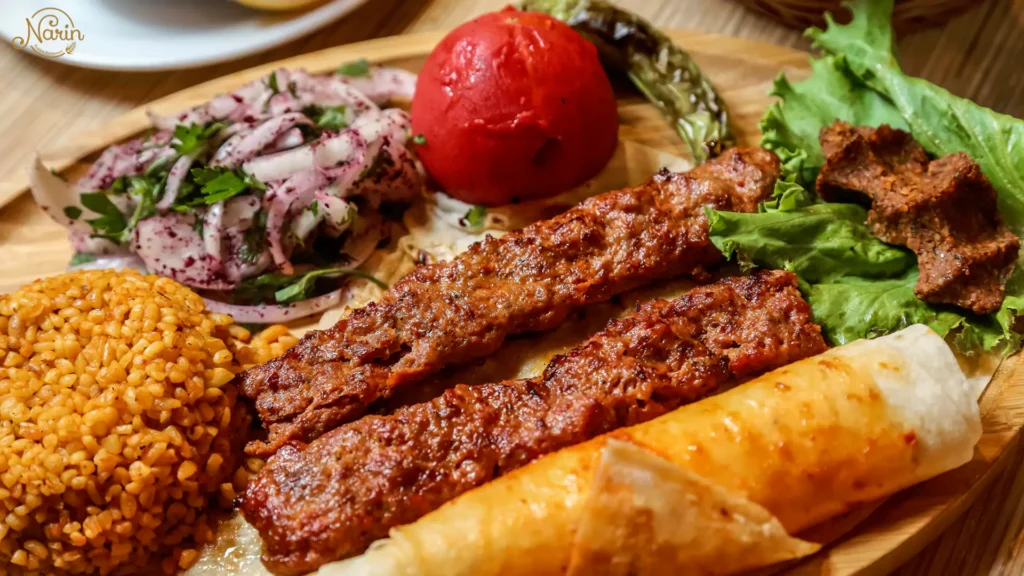 Traditional Persian Koobideh meal with two skewers of minced meat, seasoned rice, grilled tomato, and onion salad.