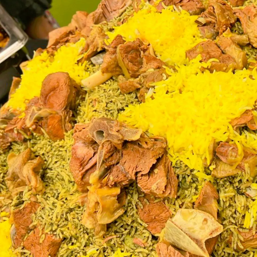 Close-up of a large catering tray at Narin Persian Restaurant in Sydney, filled with traditional Persian Baghali Polo (dill and fava bean rice), topped with tender pieces of slow-cooked meat on the bone and bright yellow saffron rice garnishes.