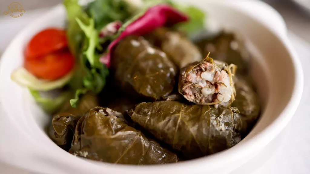 Close-up of traditional Persian vegetarian stuffed grape leaves, known as Dolmeh Barg Mo, filled with rice and herbs, served in a white bowl and garnished with a side of fresh salad at Narin Persian Restaurant.