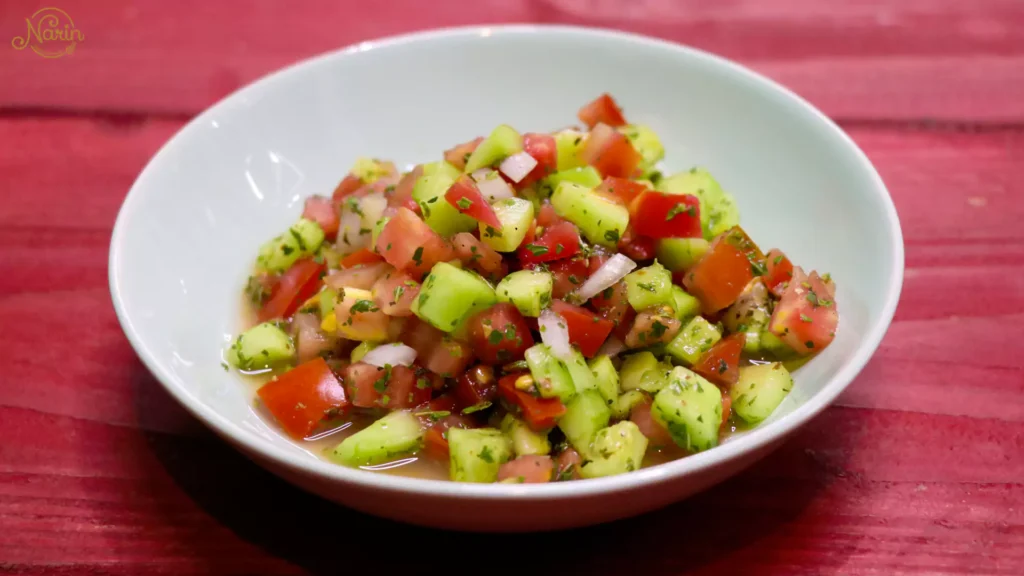 A refreshing bowl of traditional Persian Salad Shirazi at Narin Persian Restaurant in Sydney, featuring finely diced fresh cucumbers, tomatoes, and onions mixed with dried mint and a zesty dressing, served in a white bowl on a rustic red wooden table.
