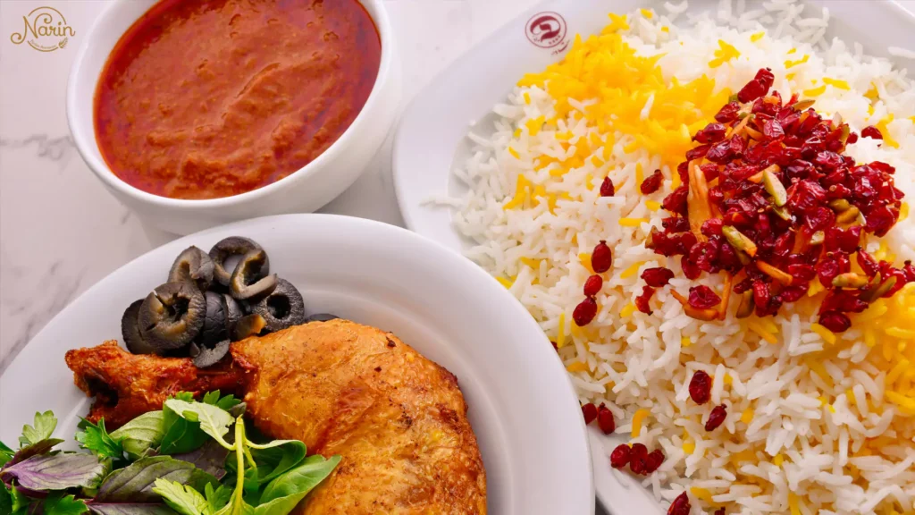 A beautiful serving of Zereshk Polo featuring saffron rice with barberries, a side of roasted chicken, and rich tomato sauce at Narin Persian Restaurant.