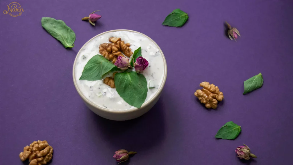 A refreshing bowl of Mast-o-Khiar (Persian yogurt and cucumber dip) garnished with walnuts and rose buds, showcasing exactly what to order at a Persian restaurant like Narin.   