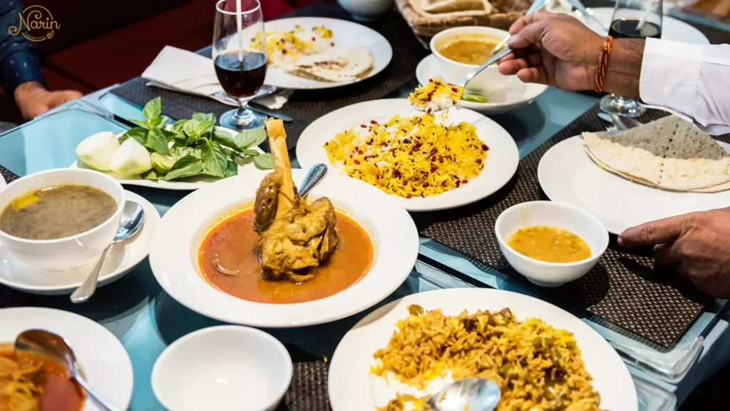 A lively dining table with people sharing lamb shank, saffron rice, and fresh herbs, showing how to eat like an Iranian at Narin Persian Restaurant.   